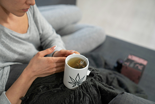 Une femme assise sur un canapé en train de savourer une tasse d'infusion au CBD